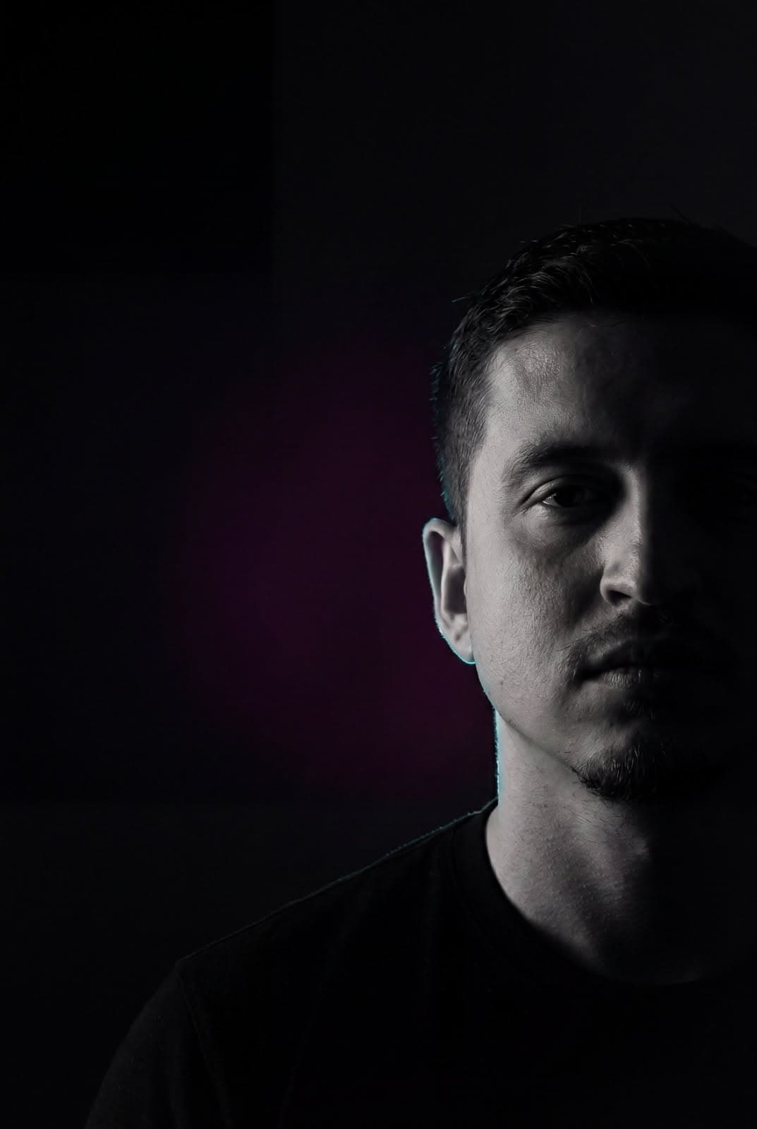 Retrato vertical de Mario Medina con camiseta negra, fondo oscuro y un lado del rostro iluminado.