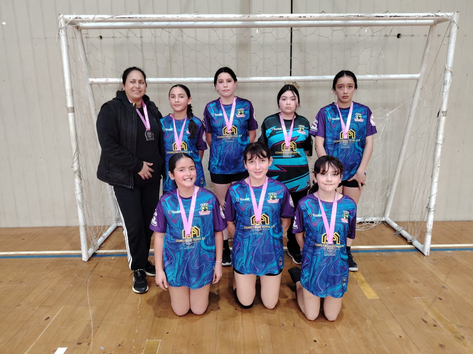 Integrantes del equipo Mini Damas de Balonmano Nacimiento con sus medallas, frente a un arco.