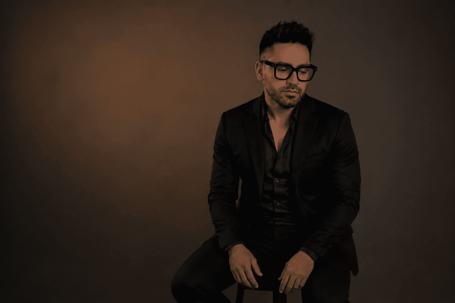 Retrato de Alejandro Shir vestido de negro y sentado frente a un fondo marrón de estudio.